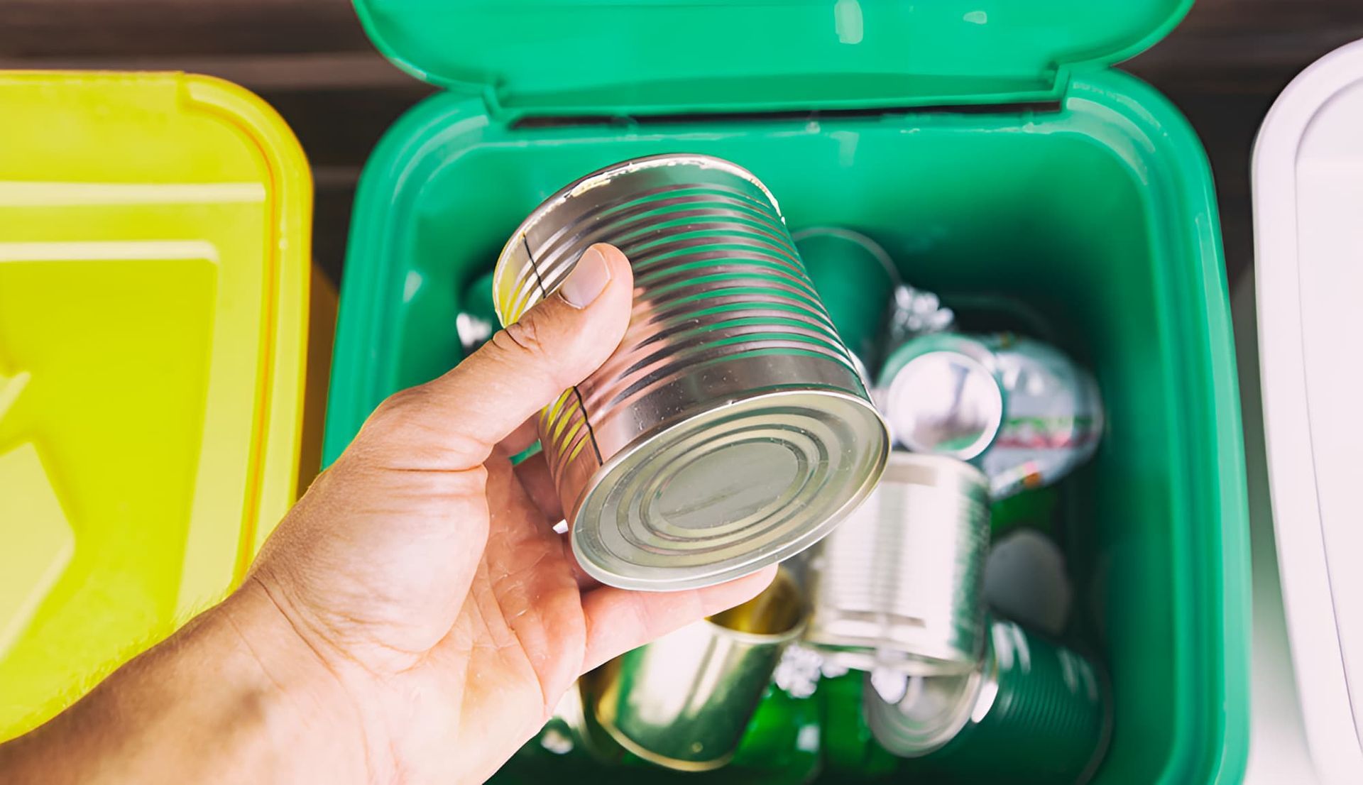 A Person Is Holding A Can In Their Hand In Front Of A Recycling Bin — North Queensland Recycling Agents In Bungalow, QLD