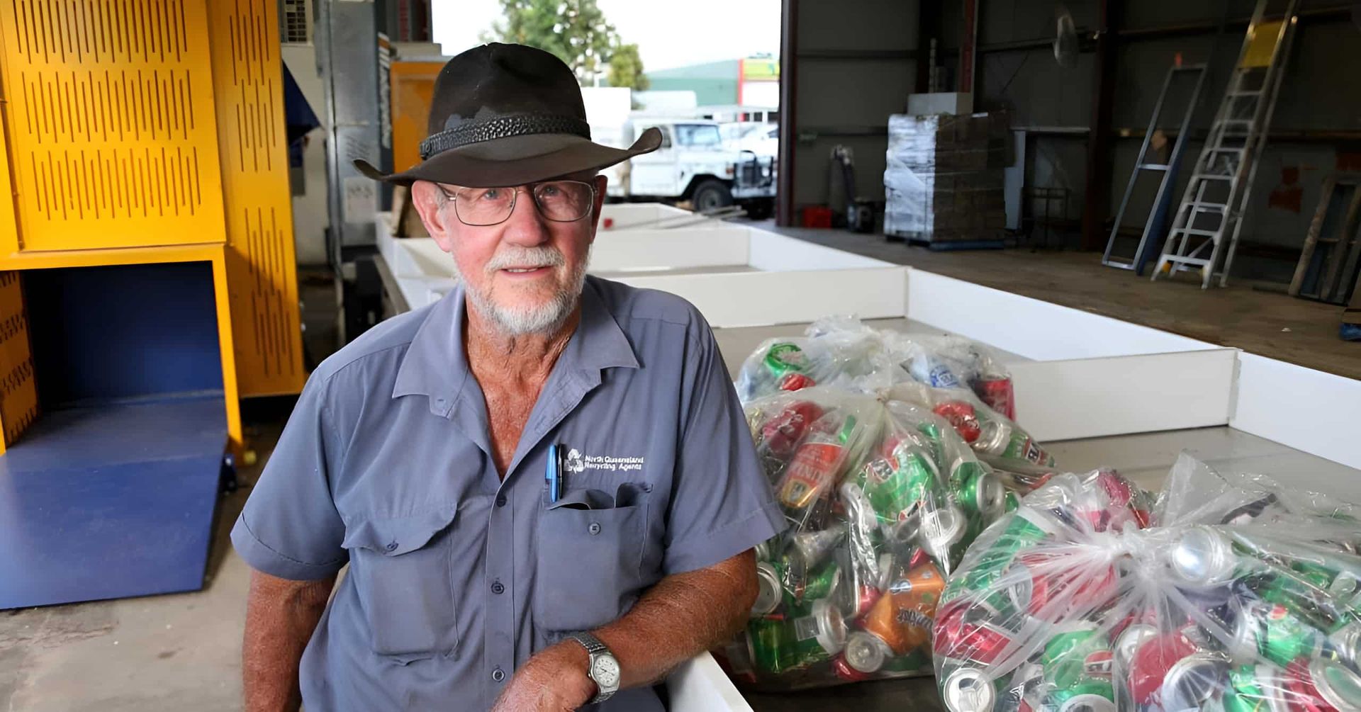 A Man In A Hat Is Standing In Front Of A Pile Of Cans — North Queensland Recycling Agents In Bungalow, QLD