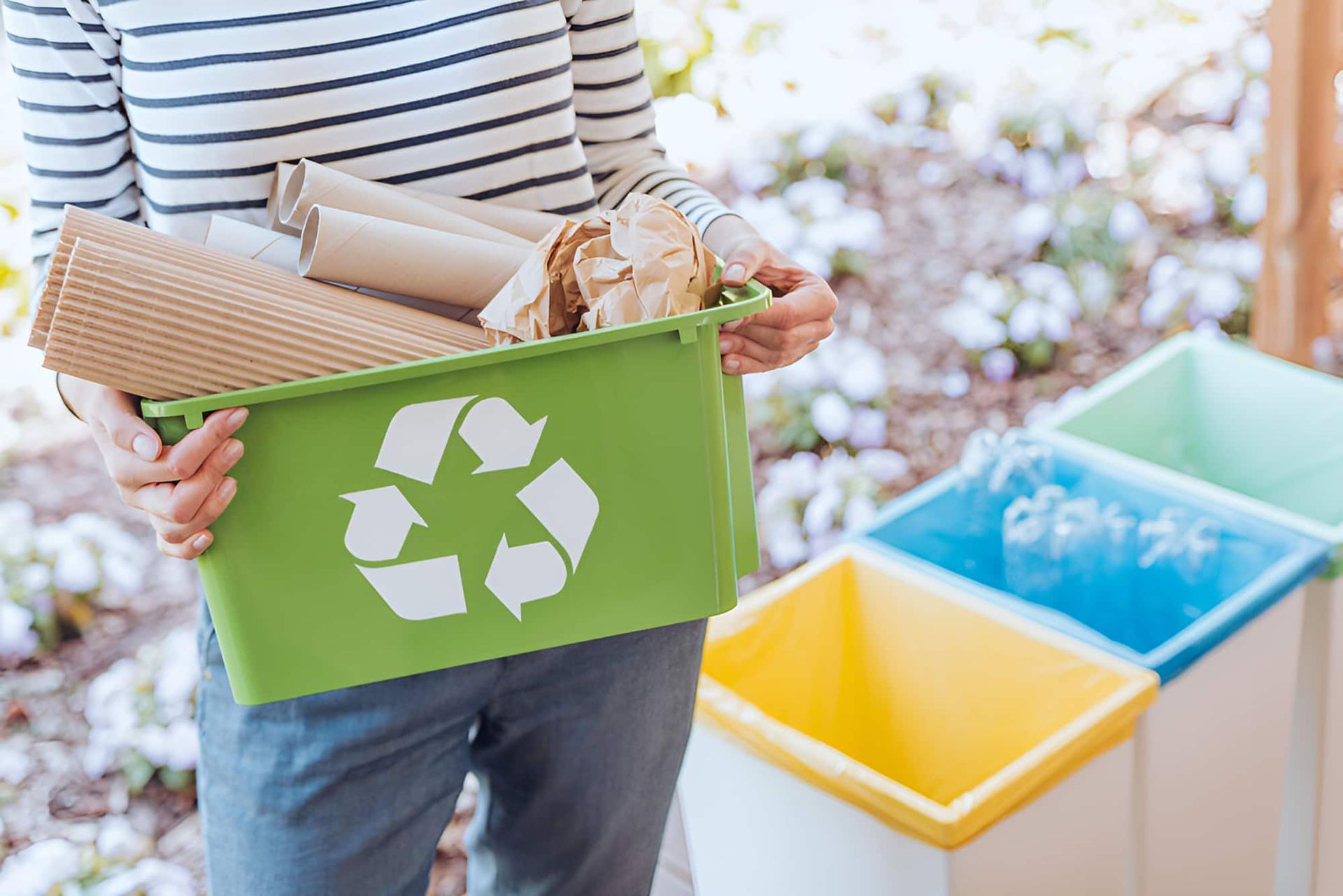 A Woman Is Holding A Green Recycling Bin Full Of Recyclables — North Queensland Recycling Agents In Bungalow, QLD