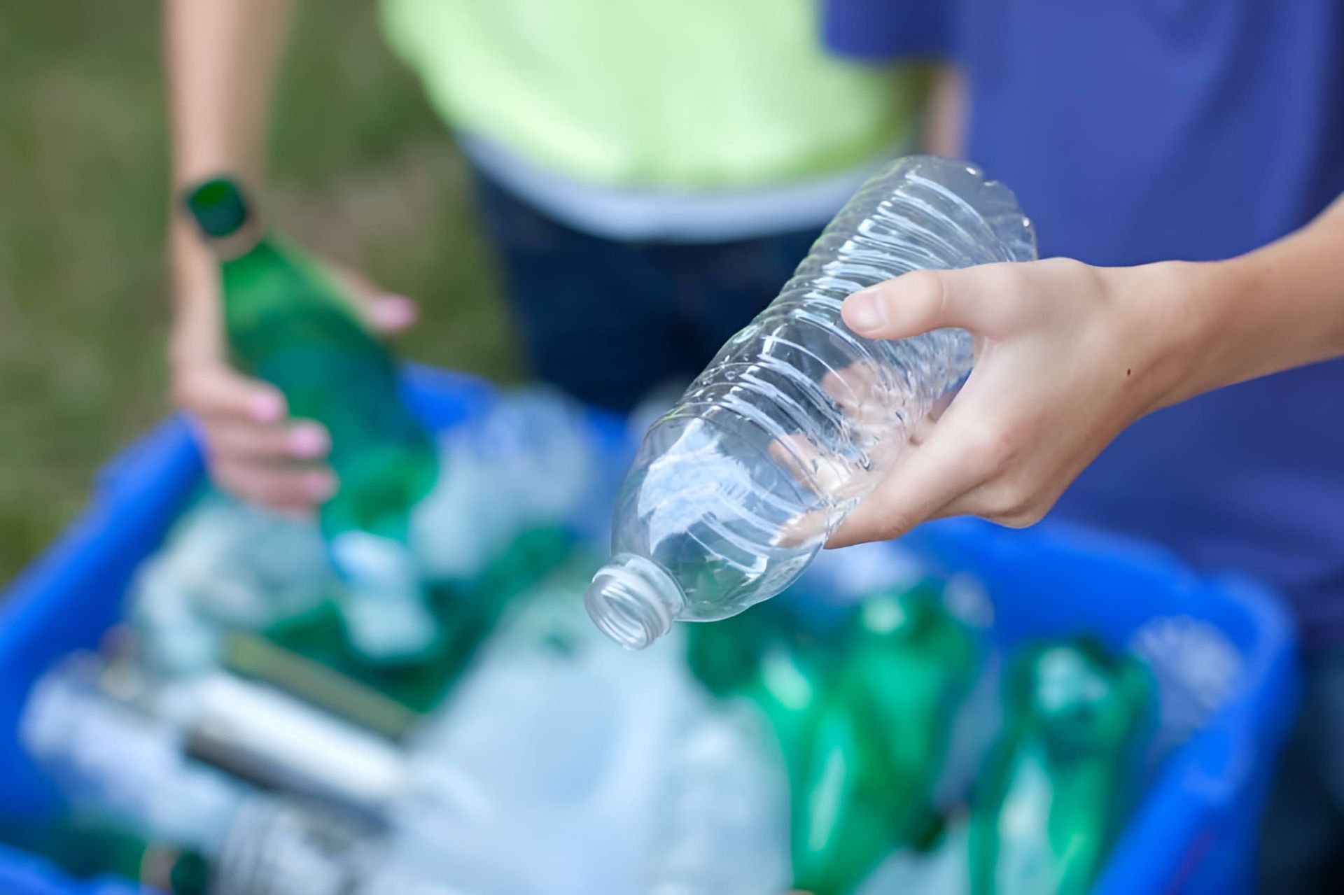 A Person Is Throwing A Plastic Bottle Into A Recycling Bin — North Queensland Recycling Agents In Bungalow, QLD