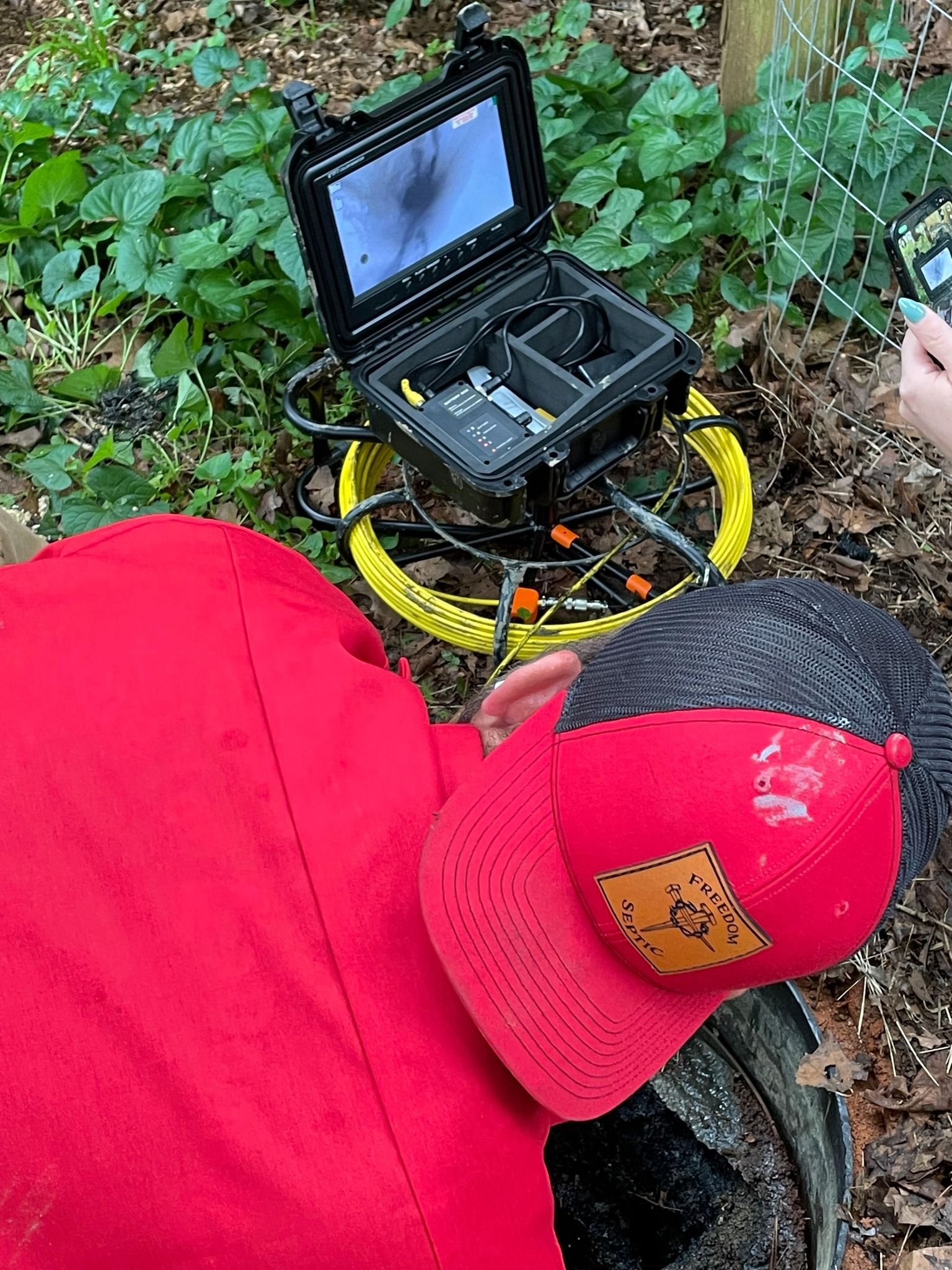 A person wearing a red hat is using a camera in the woods.