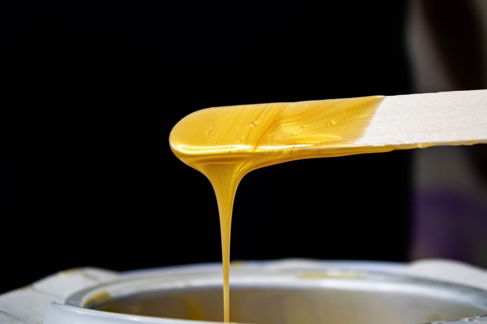 Wax is being poured from a spatula into a wax pot.