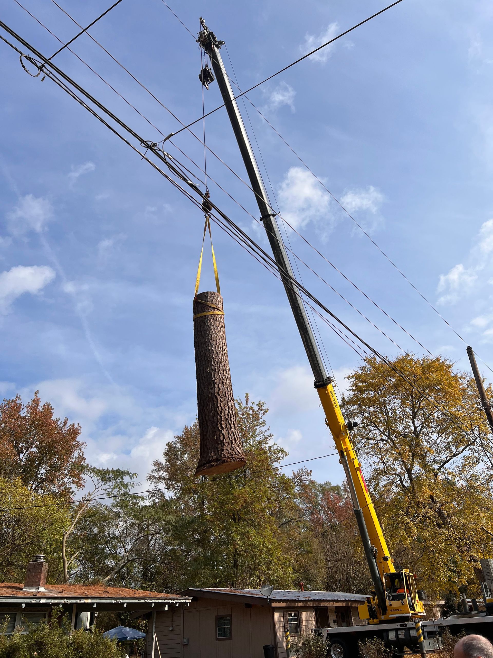 A yellow crane is lifting a very tall object over a house