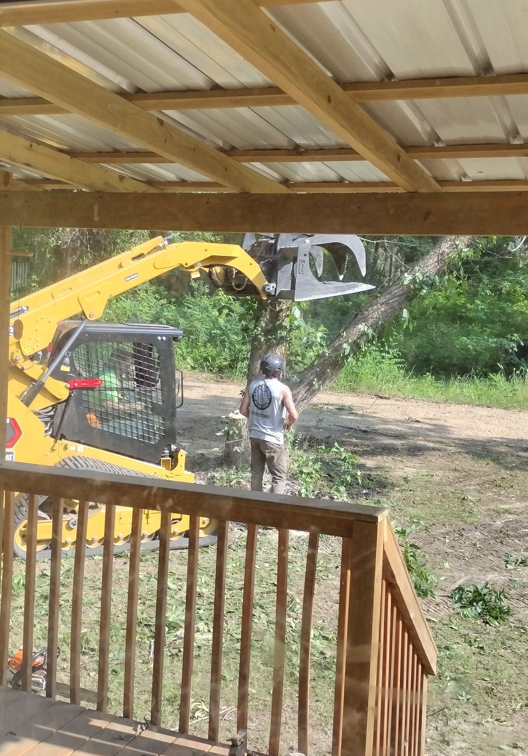 A man is standing in front of a yellow tractor cutting a tree.