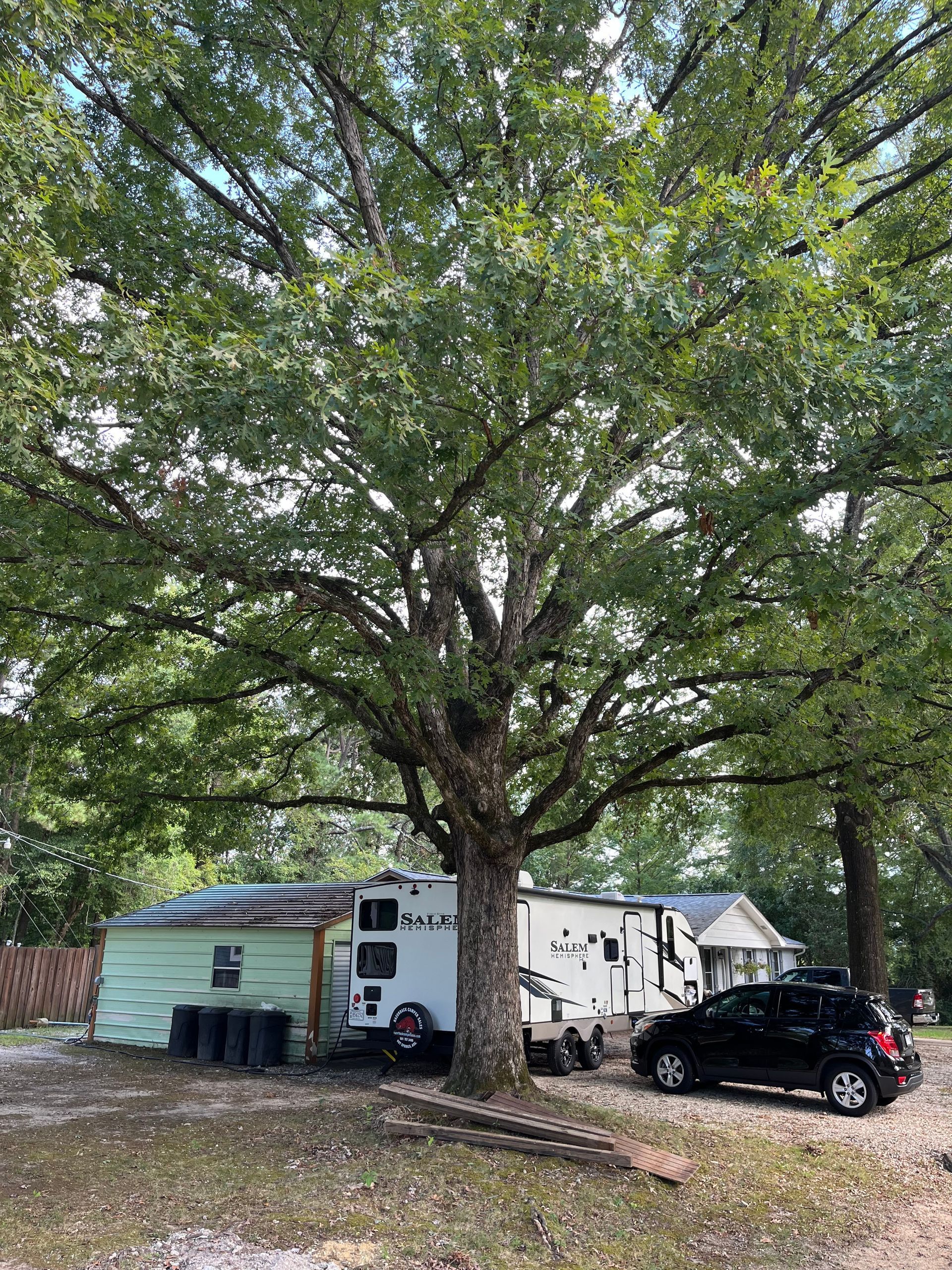 A rv is parked under a tree next to a house.