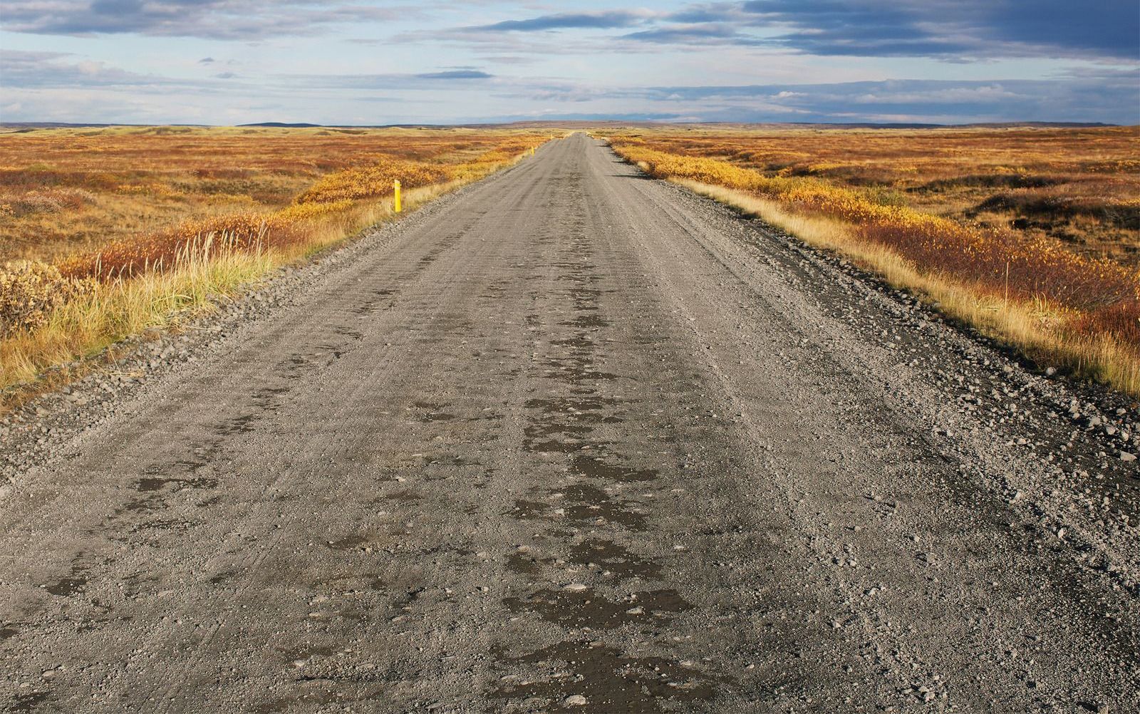A dirt road going through a dry grassy field.