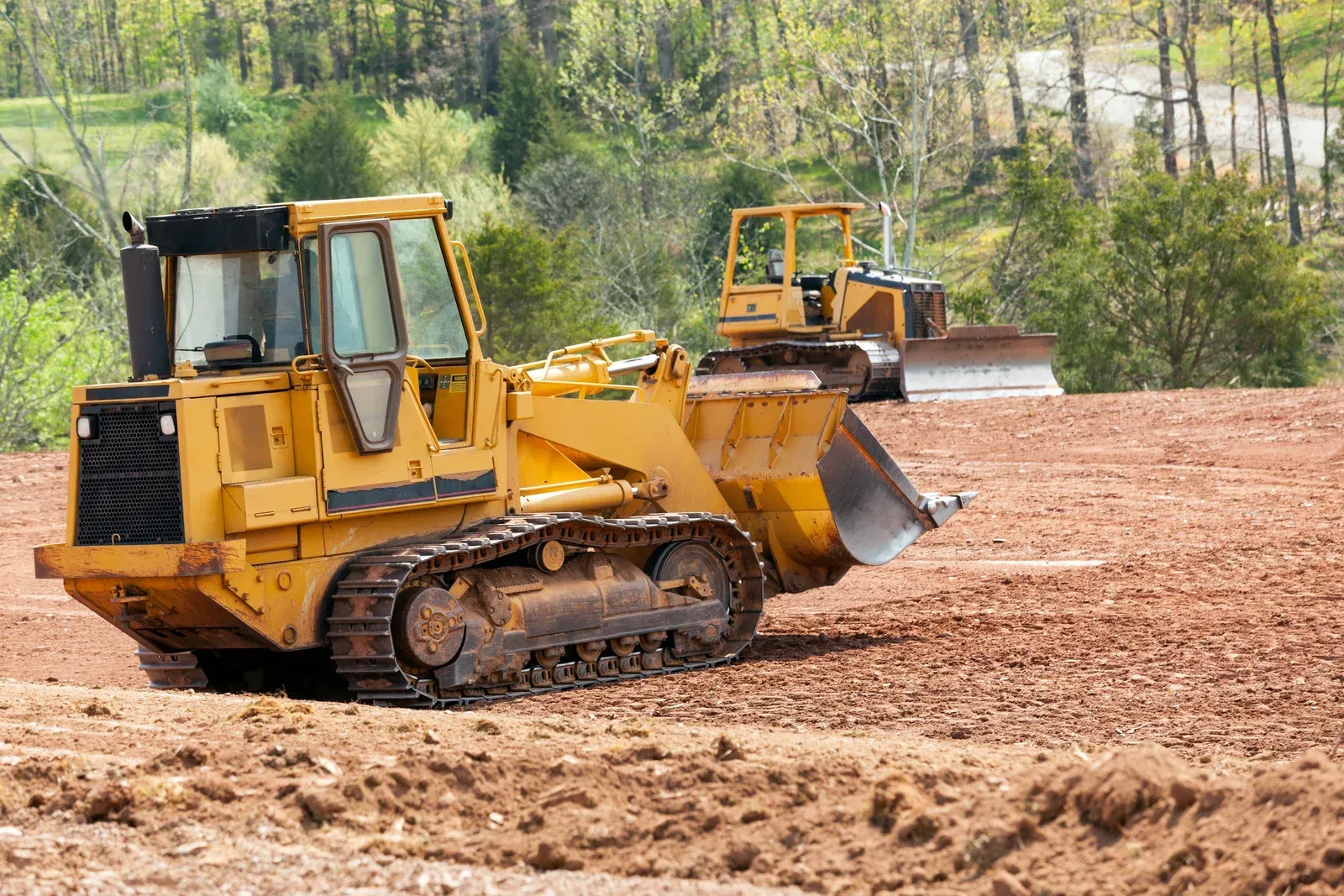 Two bulldozers are working in a dirt field.