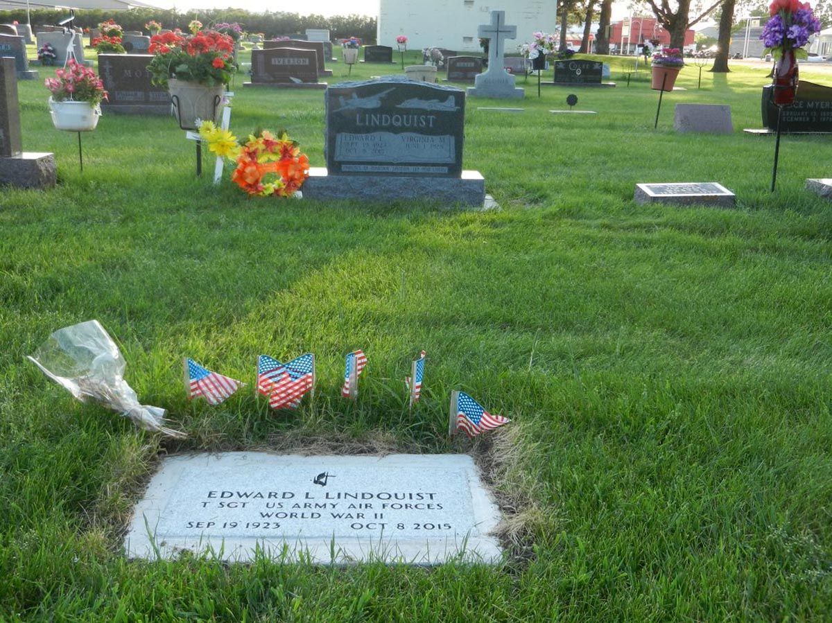 A grave in a cemetery with flags and flowers on it