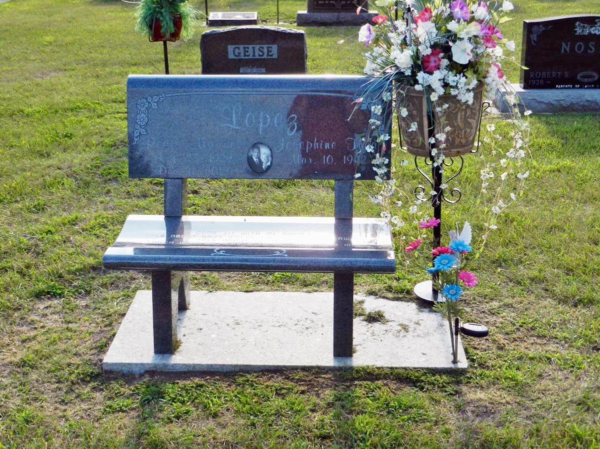 A graveyard with a bench and flowers in the grass