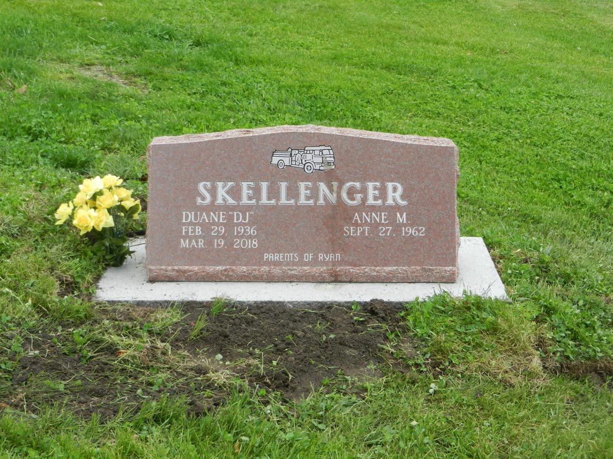 A gravestone for skellenger in a cemetery with yellow flowers