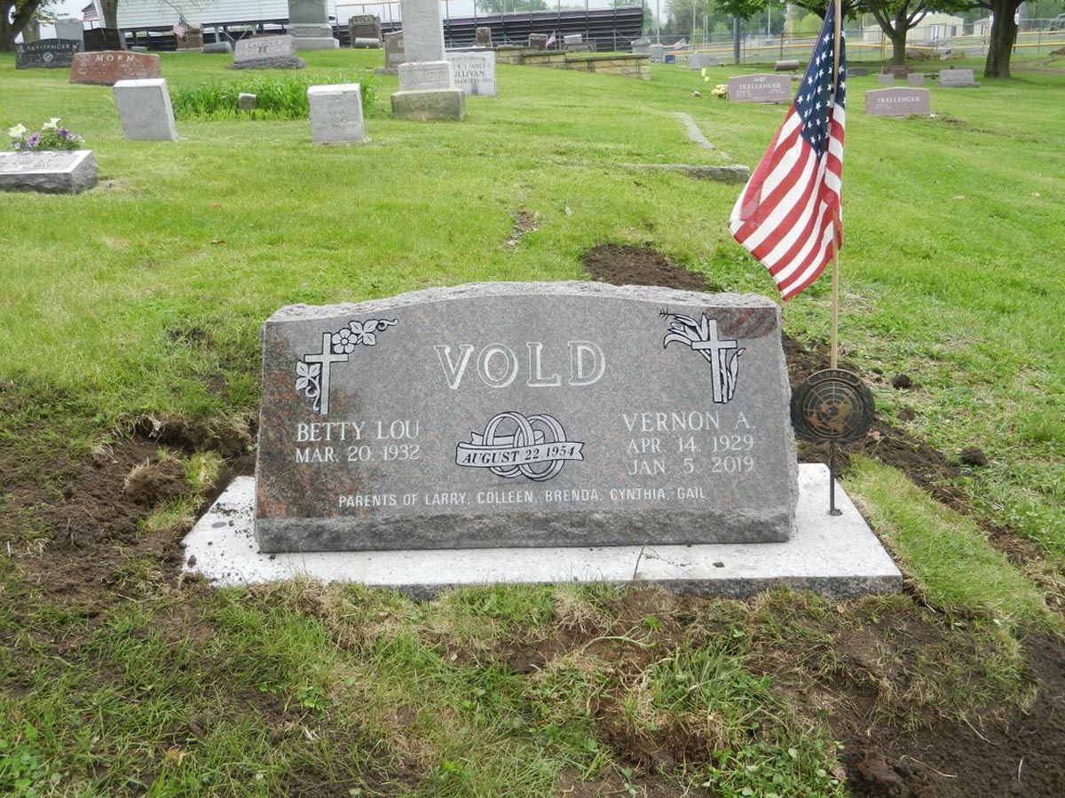 A gravestone in a cemetery with an american flag flying in the background