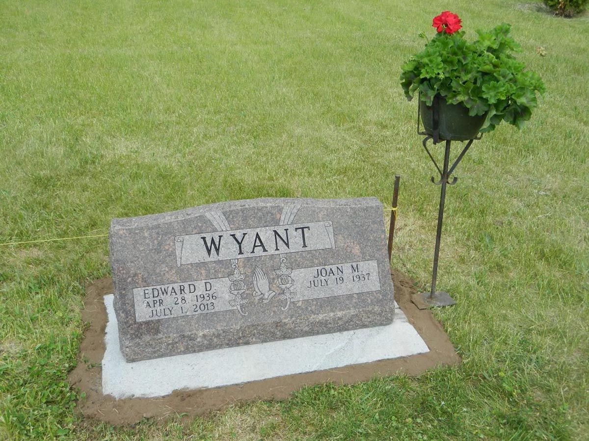 A gravestone for wyant in a cemetery with a potted plant in the background