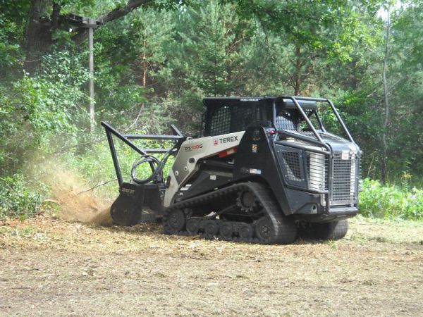 A bulldozer is driving through a field in the woods.