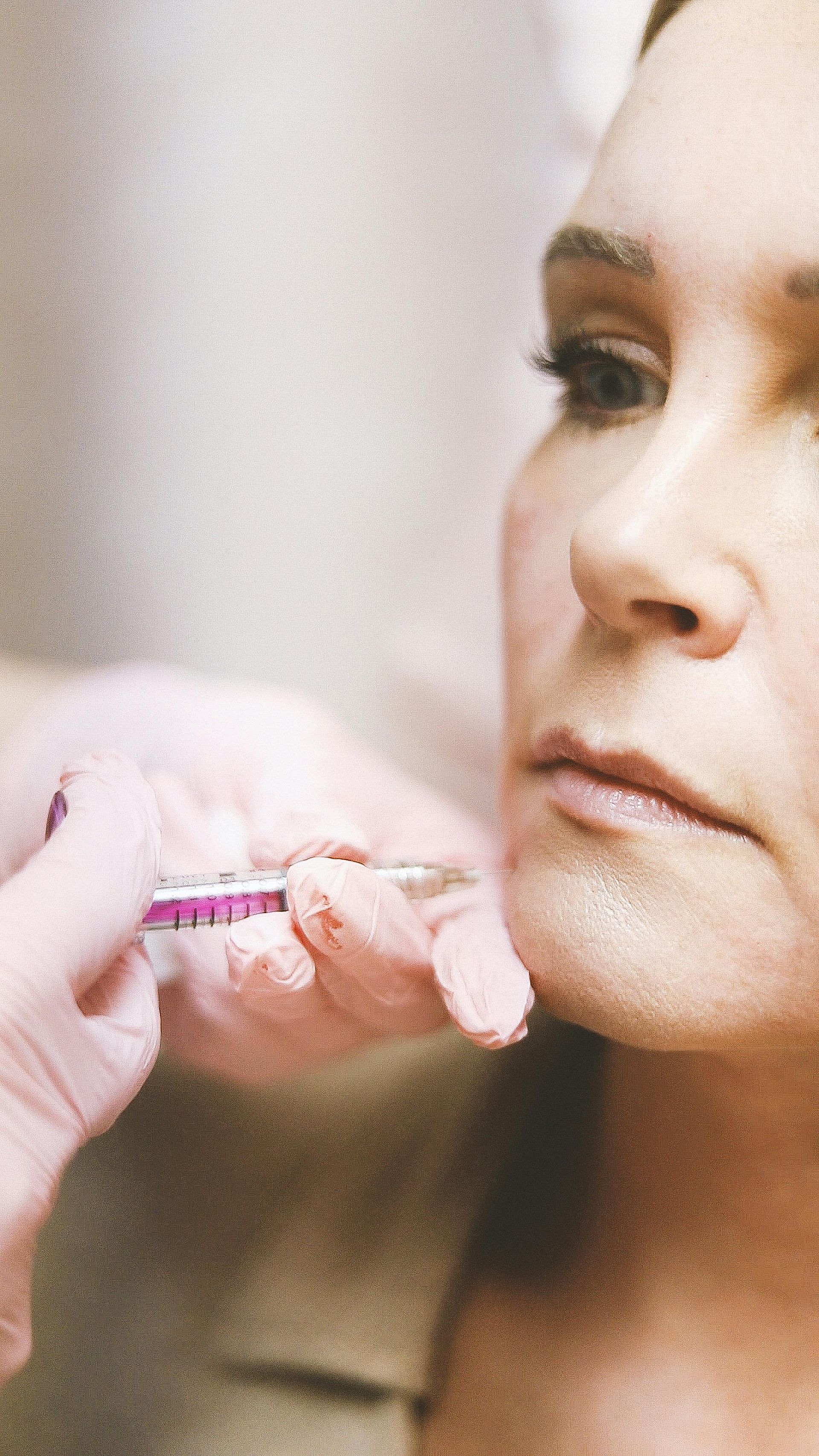Person receiving a cosmetic injection near the jawline; a gloved hand holds a syringe.