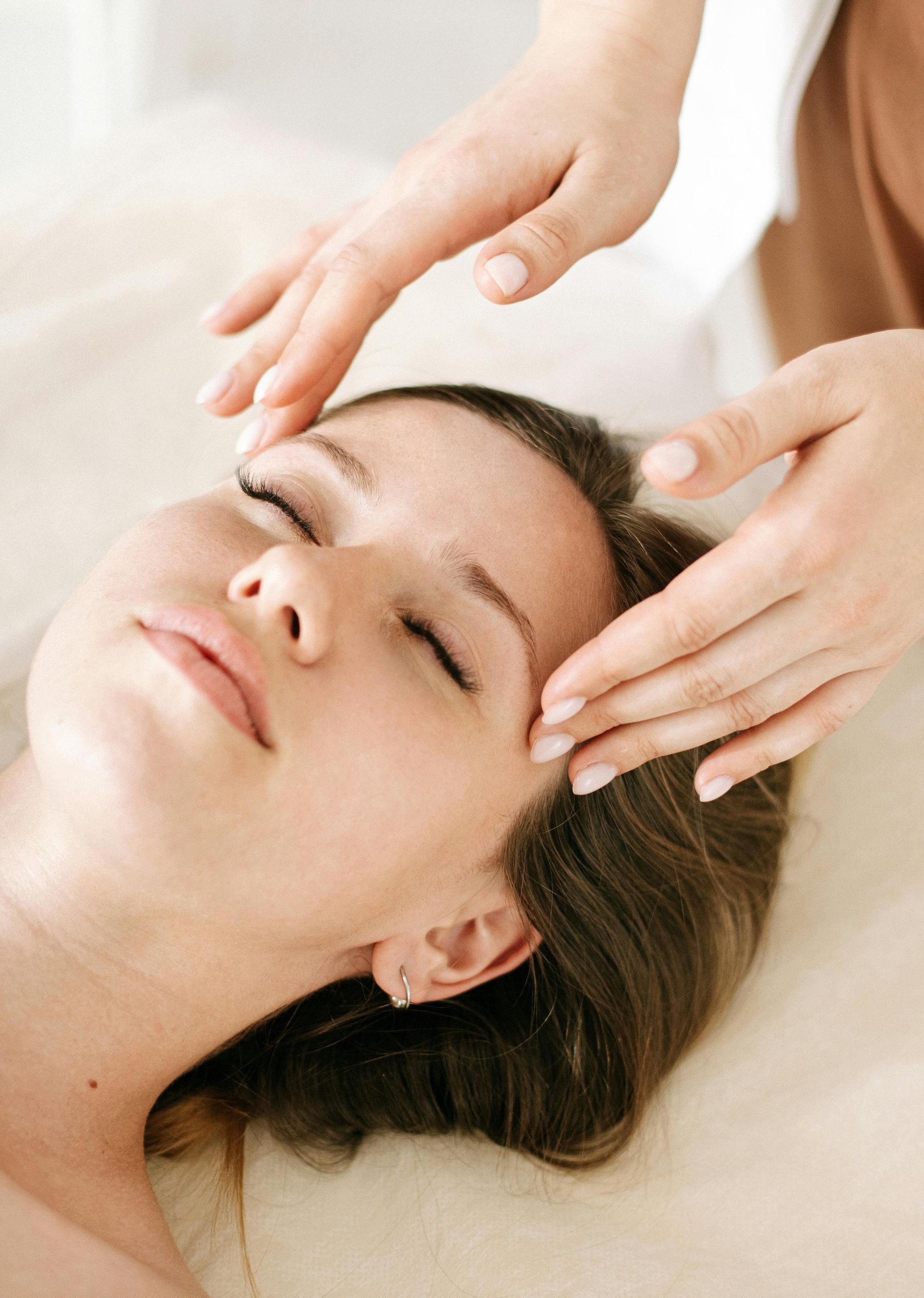 Person receiving facial massage; hands above forehead.
