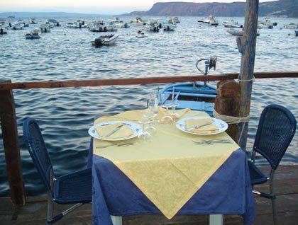 Un tavolo apparecchiato con una tovaglia gialla e blu e vista delle barche in mare