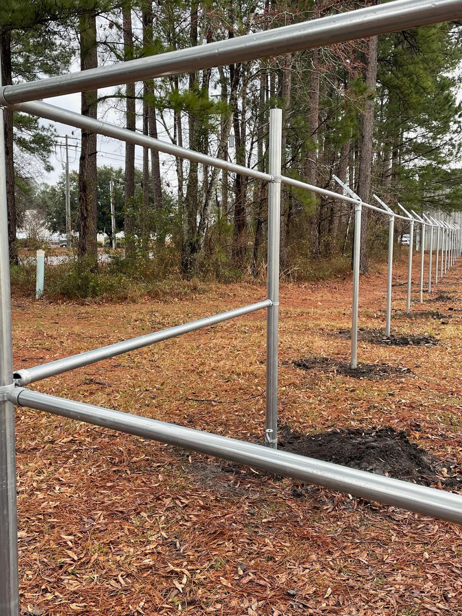 A metal fence is surrounded by trees and leaves in a field.