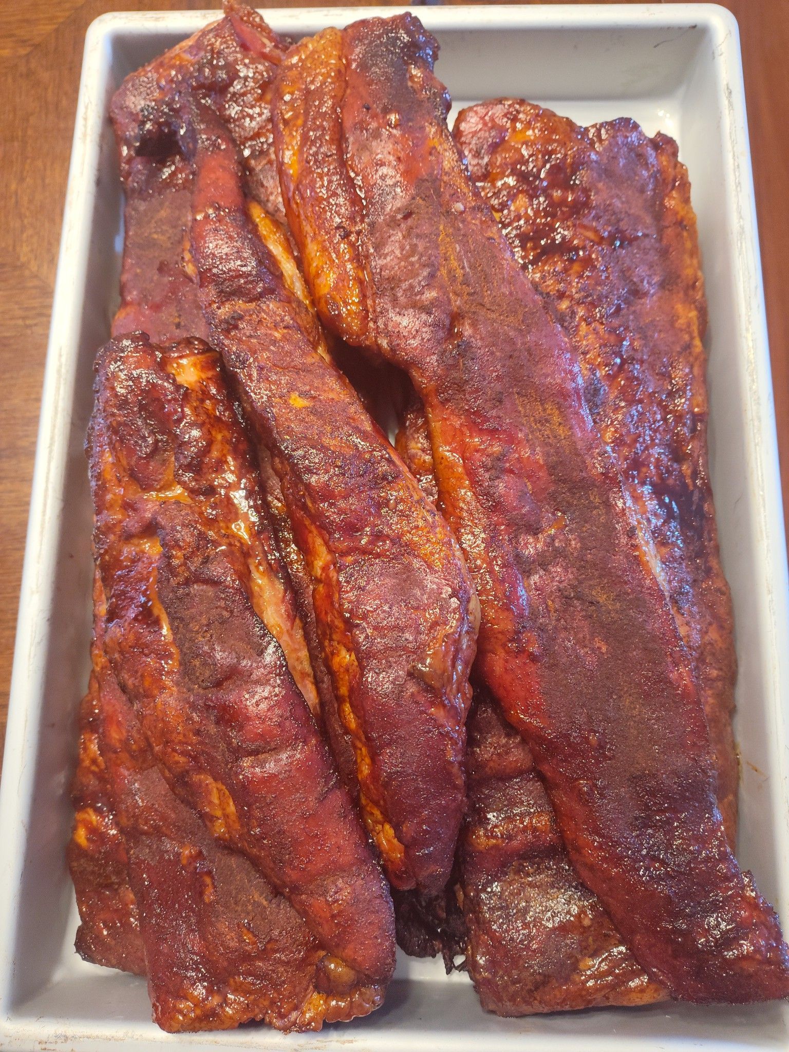 Rack of cooked ribs with a dark, reddish-brown glaze, stacked in a white rectangular dish.