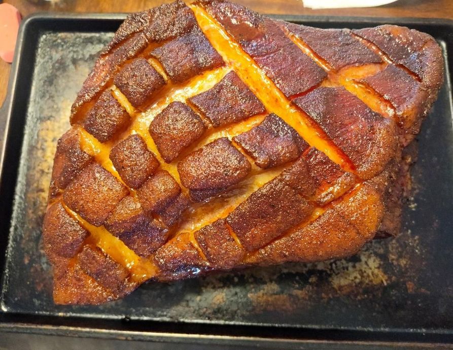 Close-up of a baked ham with a crisscross pattern on its surface, placed on a baking sheet.