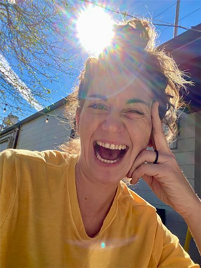 a woman in a yellow shirt is laughing with the sun shining through her hair .