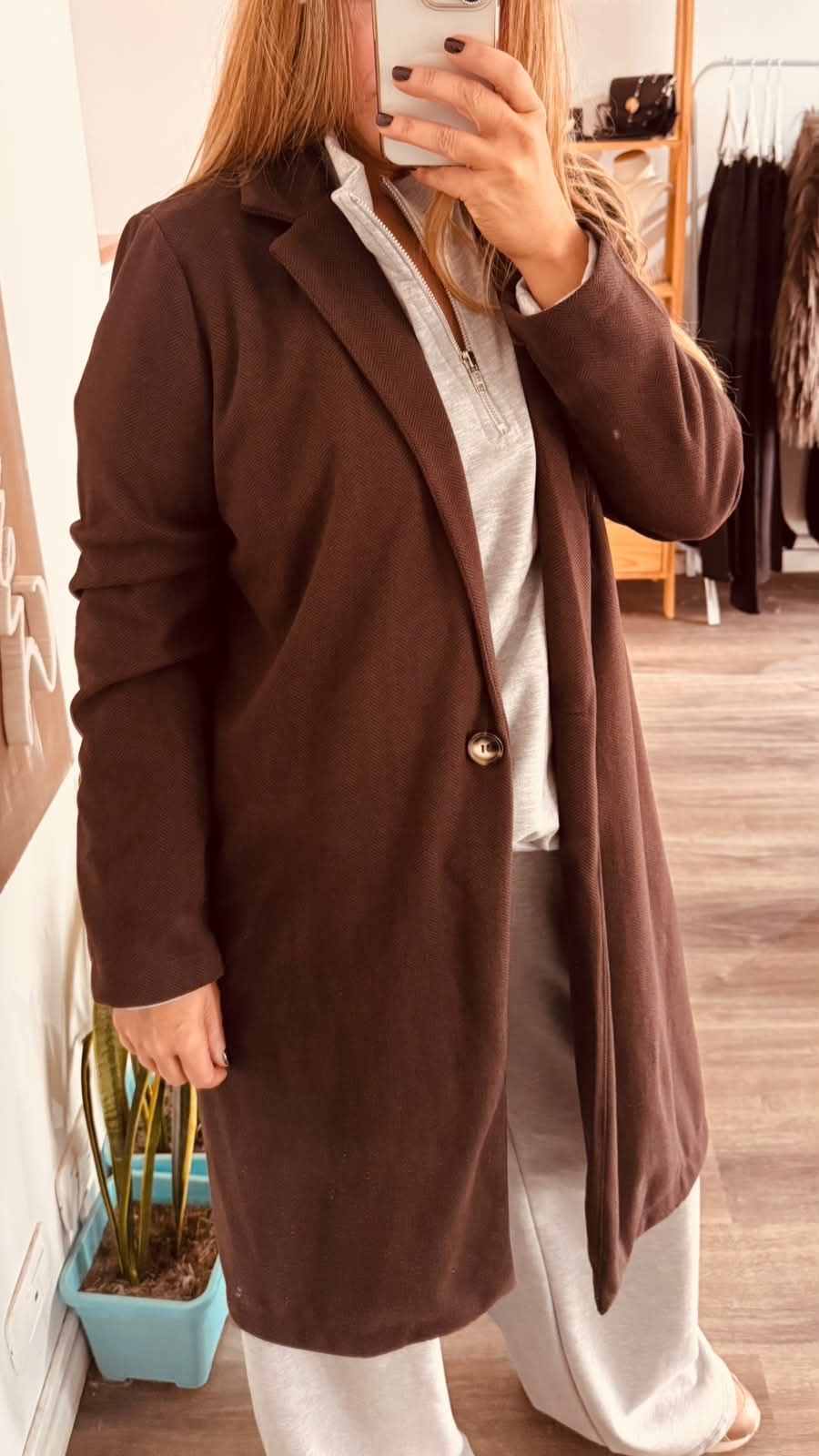 Una persona con un abrigo beige se toma una selfie frente al espejo en una tienda de ropa.