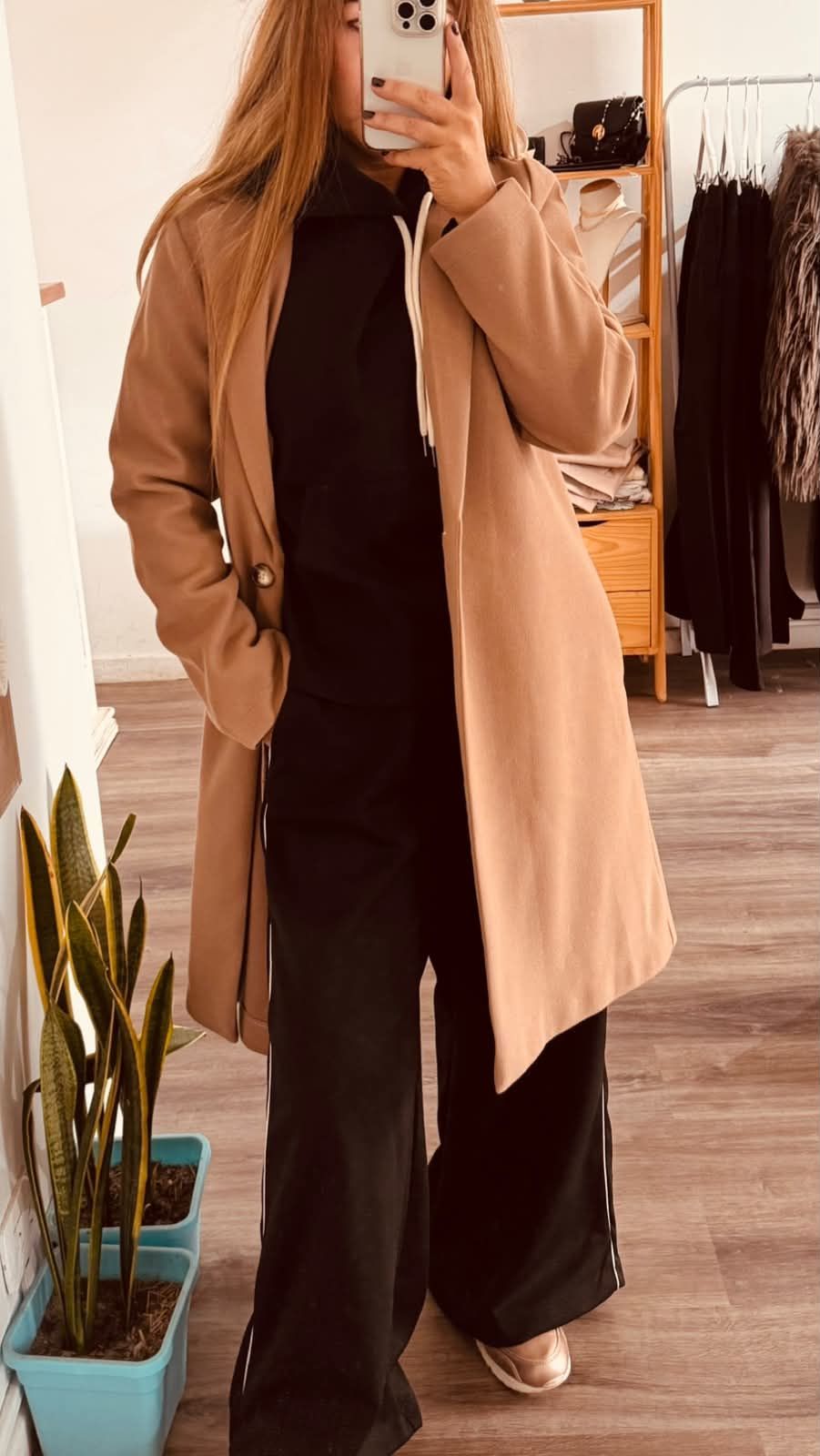 Persona tomándose una selfie frente al espejo, vestida con un abrigo color canela y pantalones oscuros.