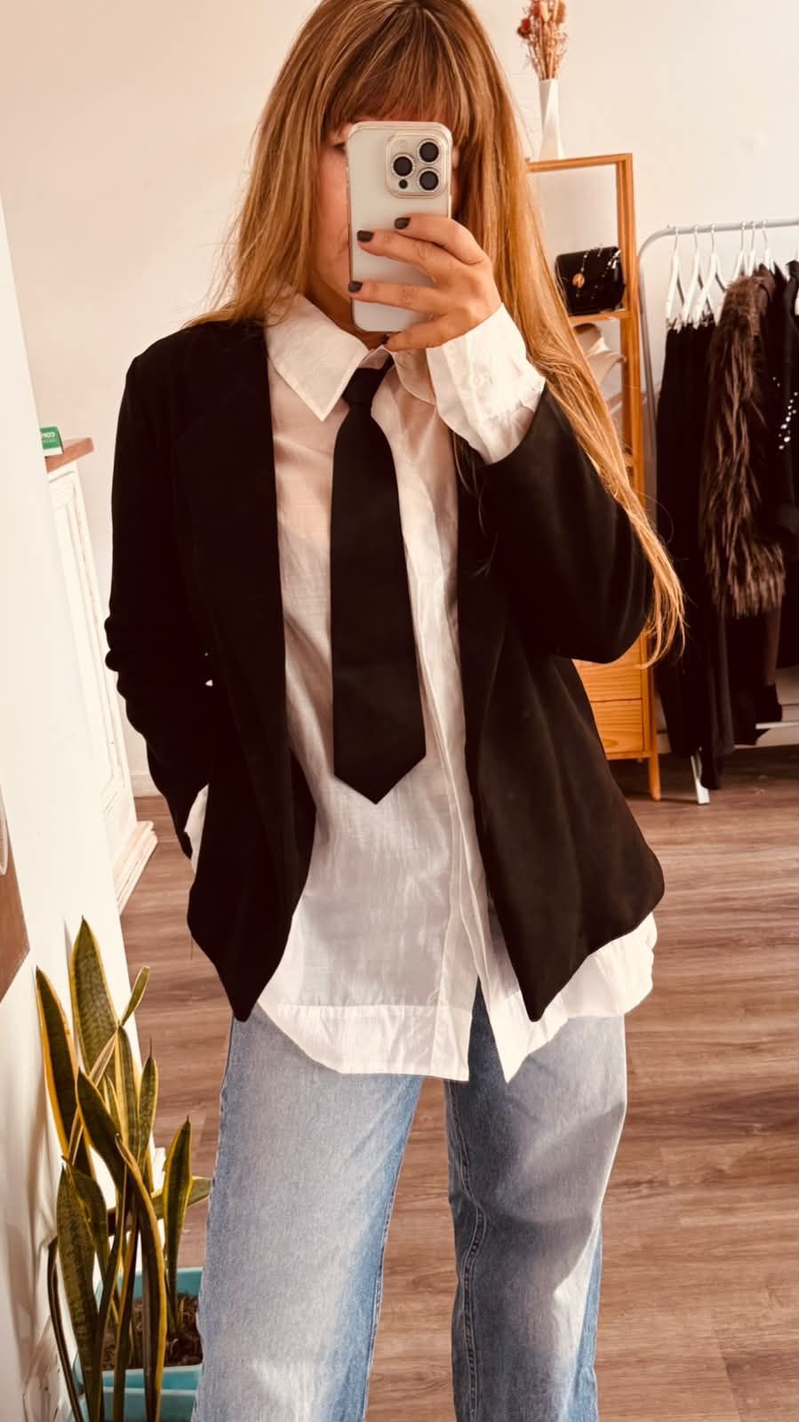 Persona tomándose una selfie frente al espejo con una camisa blanca extragrande, corbata negra y jeans azul claro.