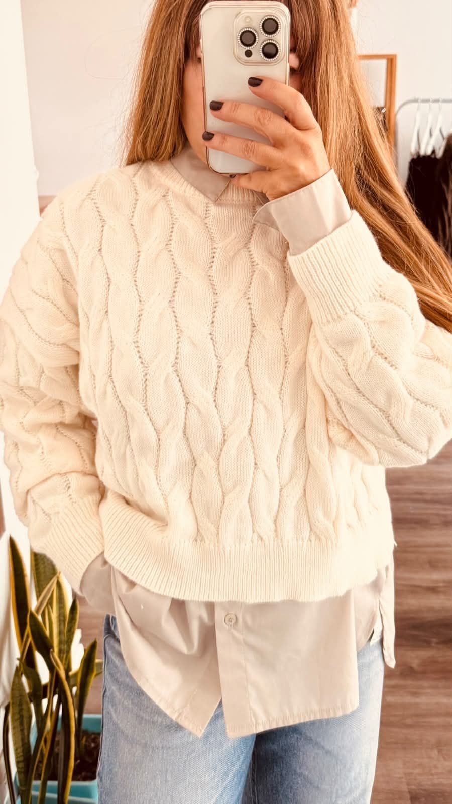 Persona tomándose una selfie frente al espejo con un suéter de punto trenzado color crema y jeans azul claro.