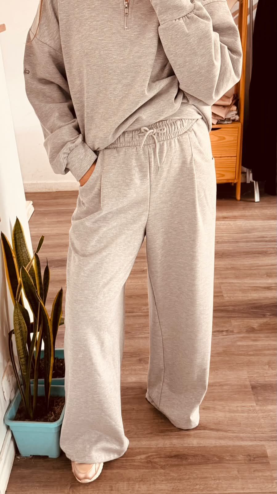 Una persona se toma una selfie frente al espejo, vestida con una sudadera gris con capucha y pantalones deportivos,.