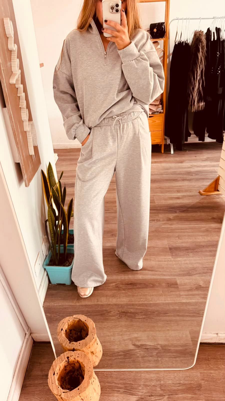 Una persona se toma una selfie frente al espejo, vestida con una sudadera gris con capucha y pantalones deportivos,.