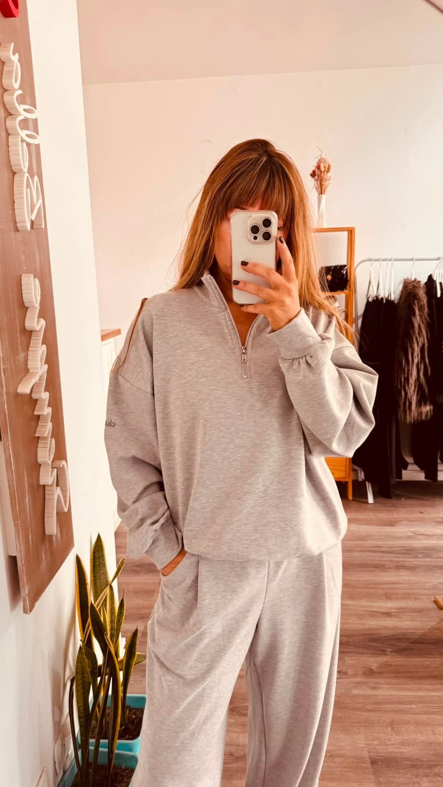 Una persona se toma una selfie frente al espejo en una habitación luminosa, vestida con una sudadera.