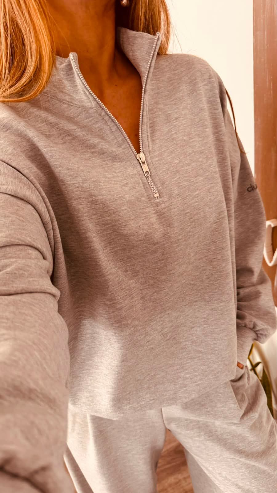 Una persona se toma una selfie frente al espejo en una habitación luminosa, vestida con una sudadera.