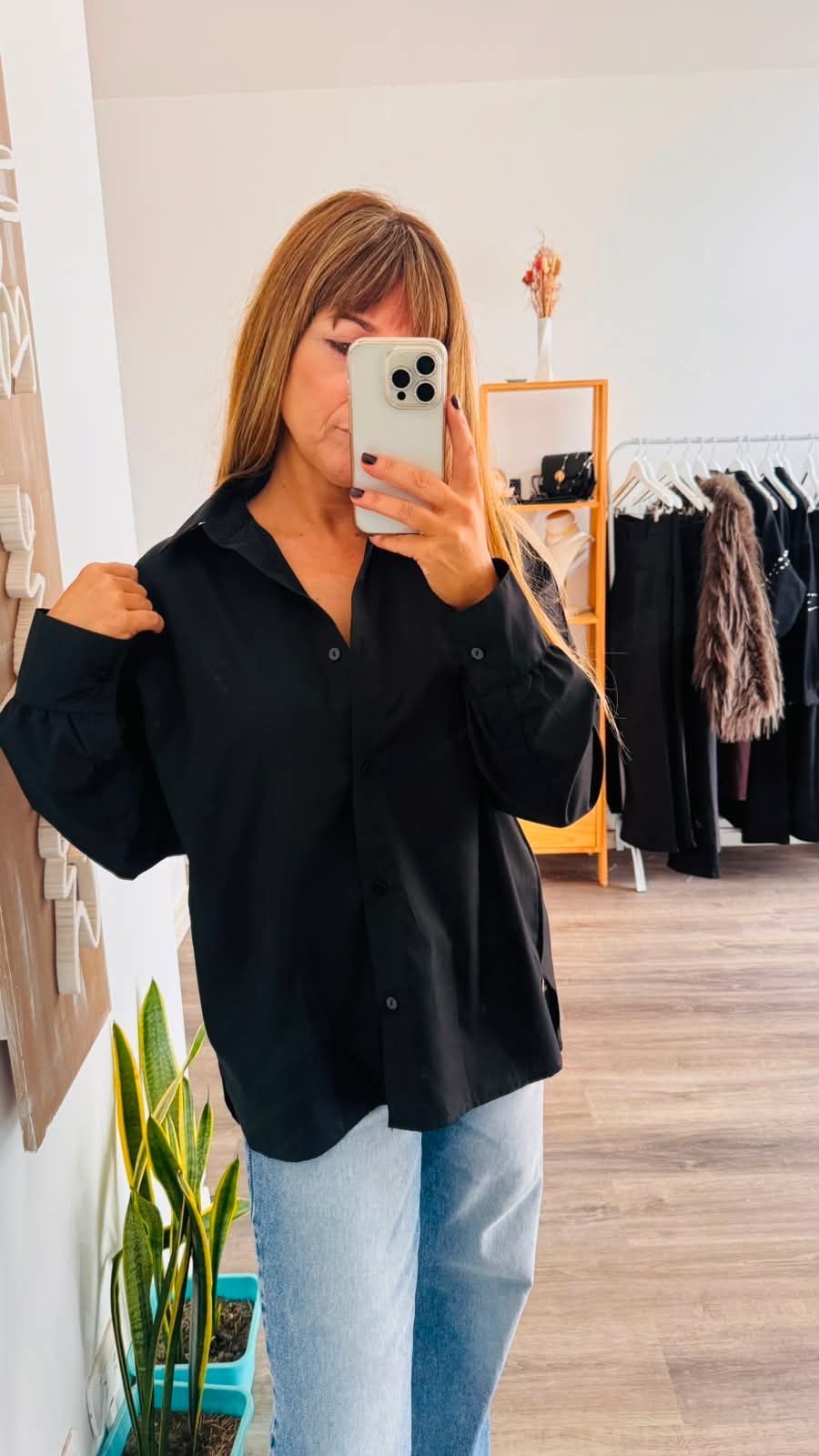 Una persona se toma una selfie frente al espejo, vestida con una camisa beige y jeans oscuros, mientras está de pie .