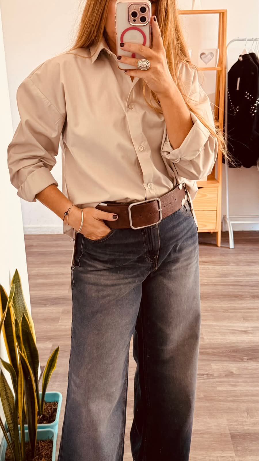 Una persona se toma una selfie frente al espejo, vestida con una camisa beige y jeans oscuros, mientras está de pie .