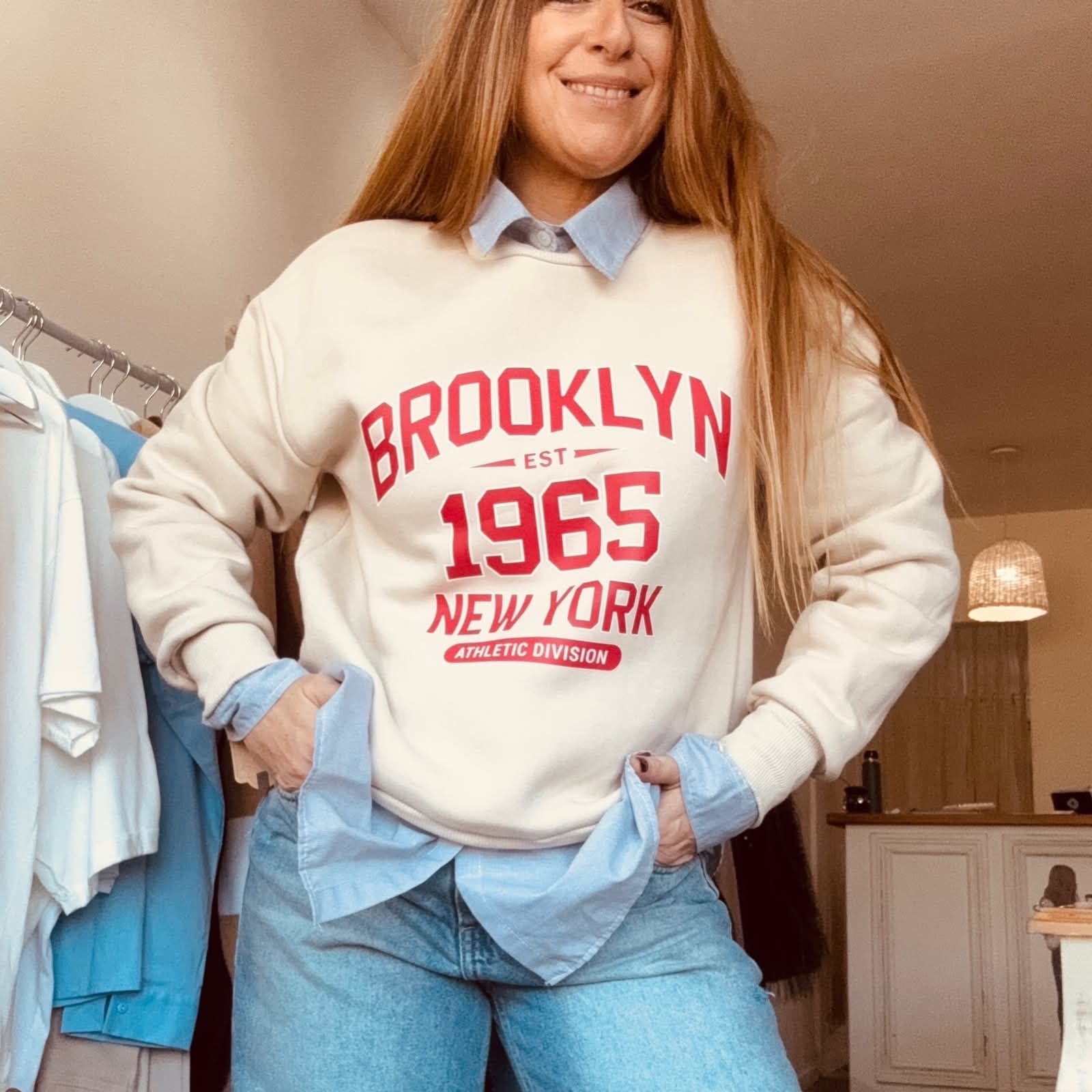 Mujer luciendo una sudadera color crema de Brooklyn 1965 con vaqueros en interiores.