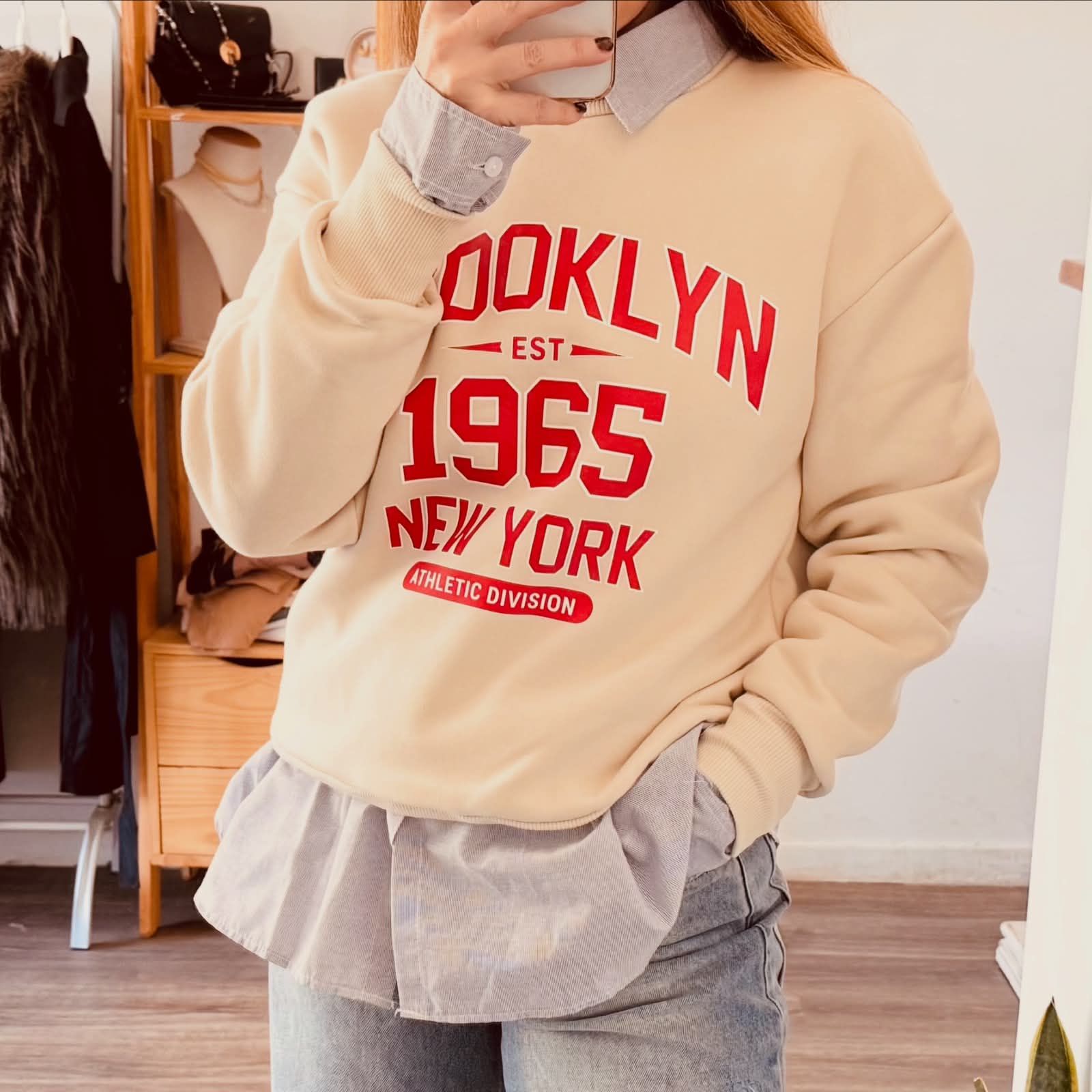 Mujer luciendo una sudadera color crema de Brooklyn 1965 con vaqueros en interiores.