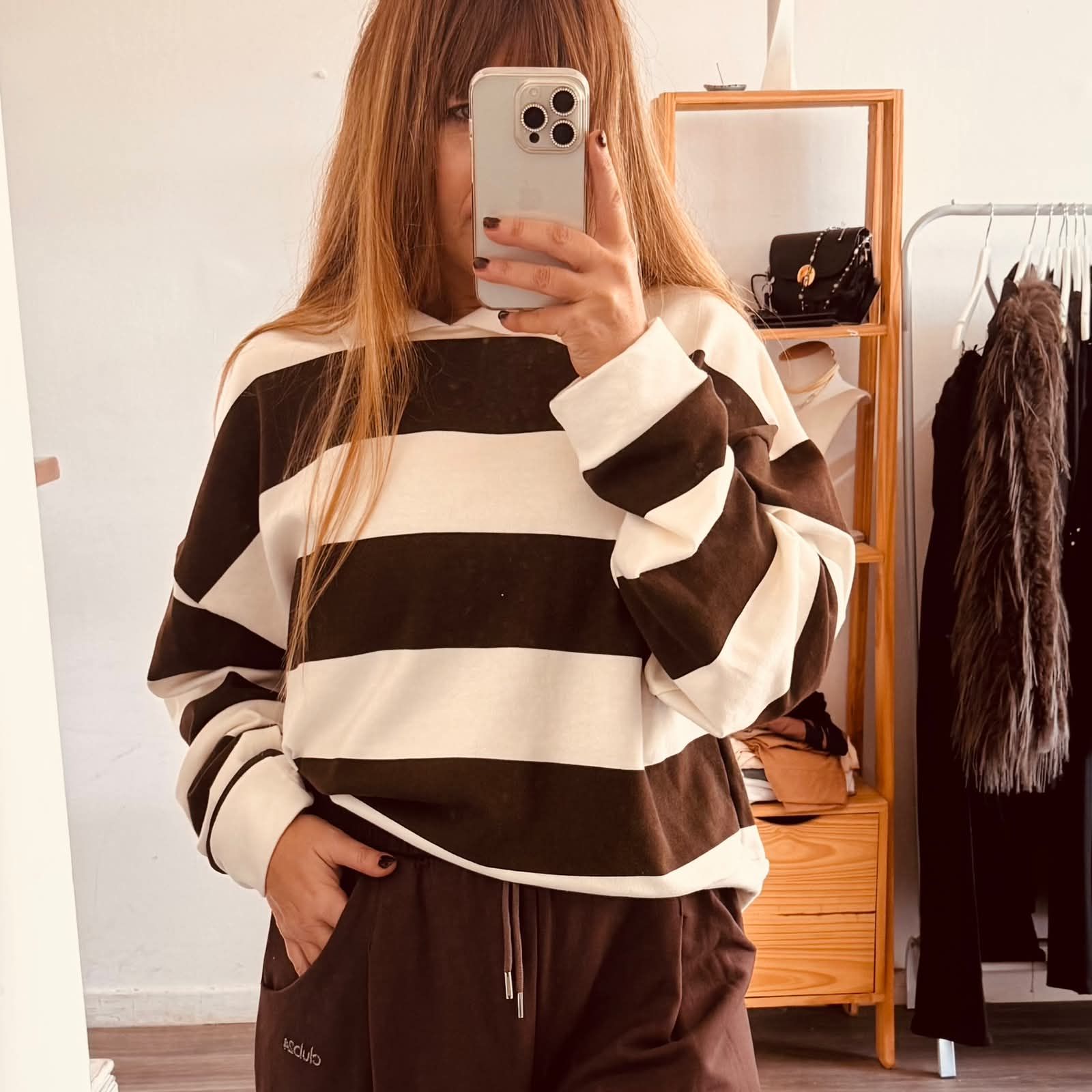 Selfie frente al espejo de una persona con un suéter y pantalones a rayas marrones y crema en un vestidor.