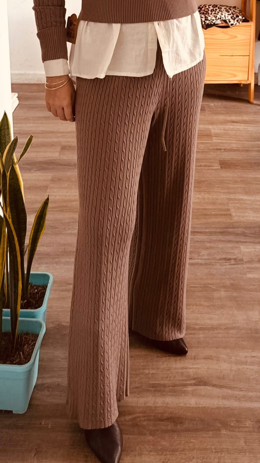 Persona vestida con un conjunto de punto marrón, una blusa blanca de varias capas y tacones de punta.