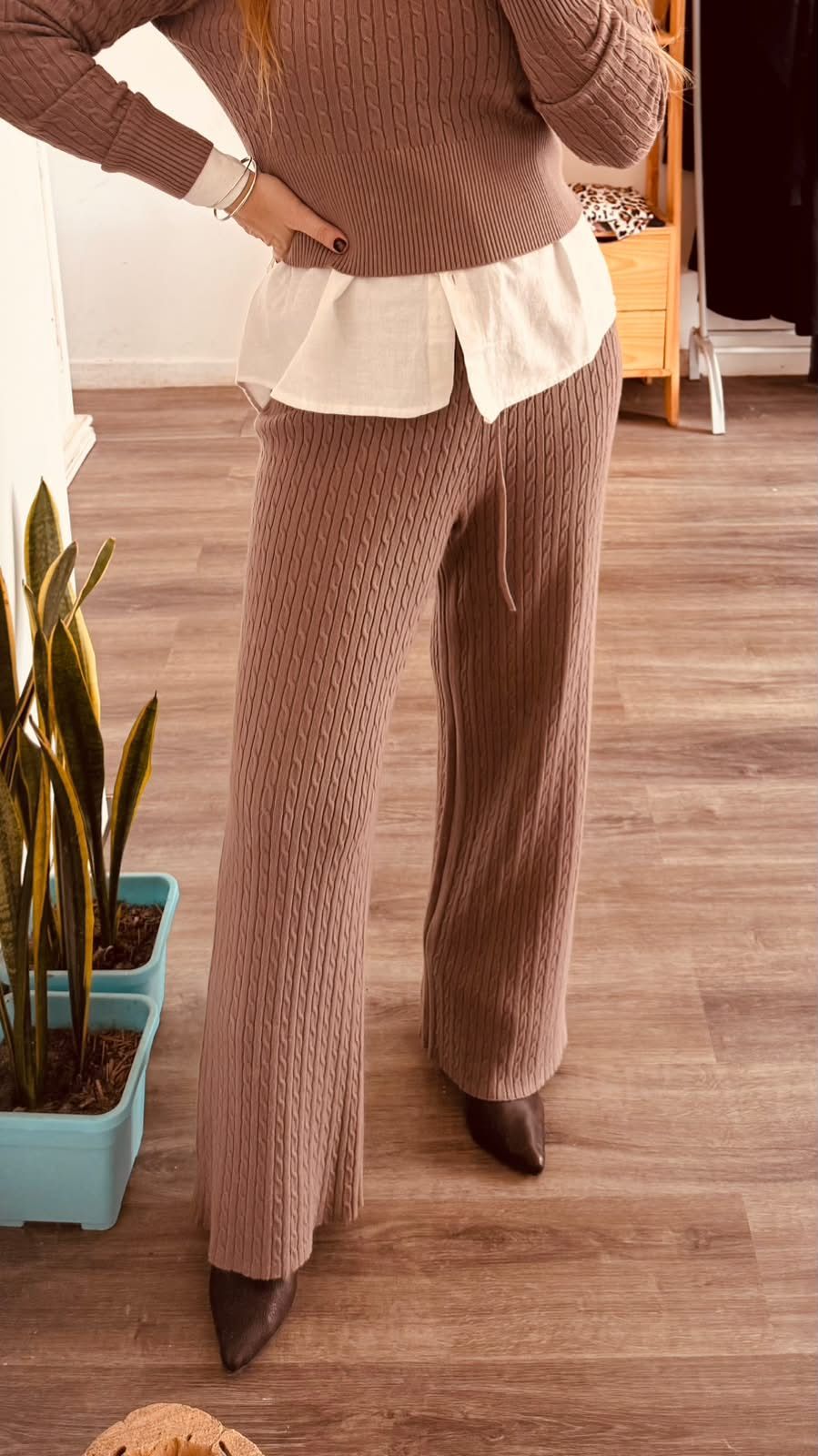 Persona vestida con un conjunto de punto marrón, una blusa blanca de varias capas y tacones de punta.