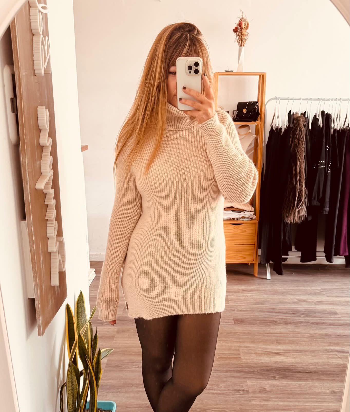 Una persona se toma una selfie frente al espejo con un vestido de punto beige, cinturón marrón,.