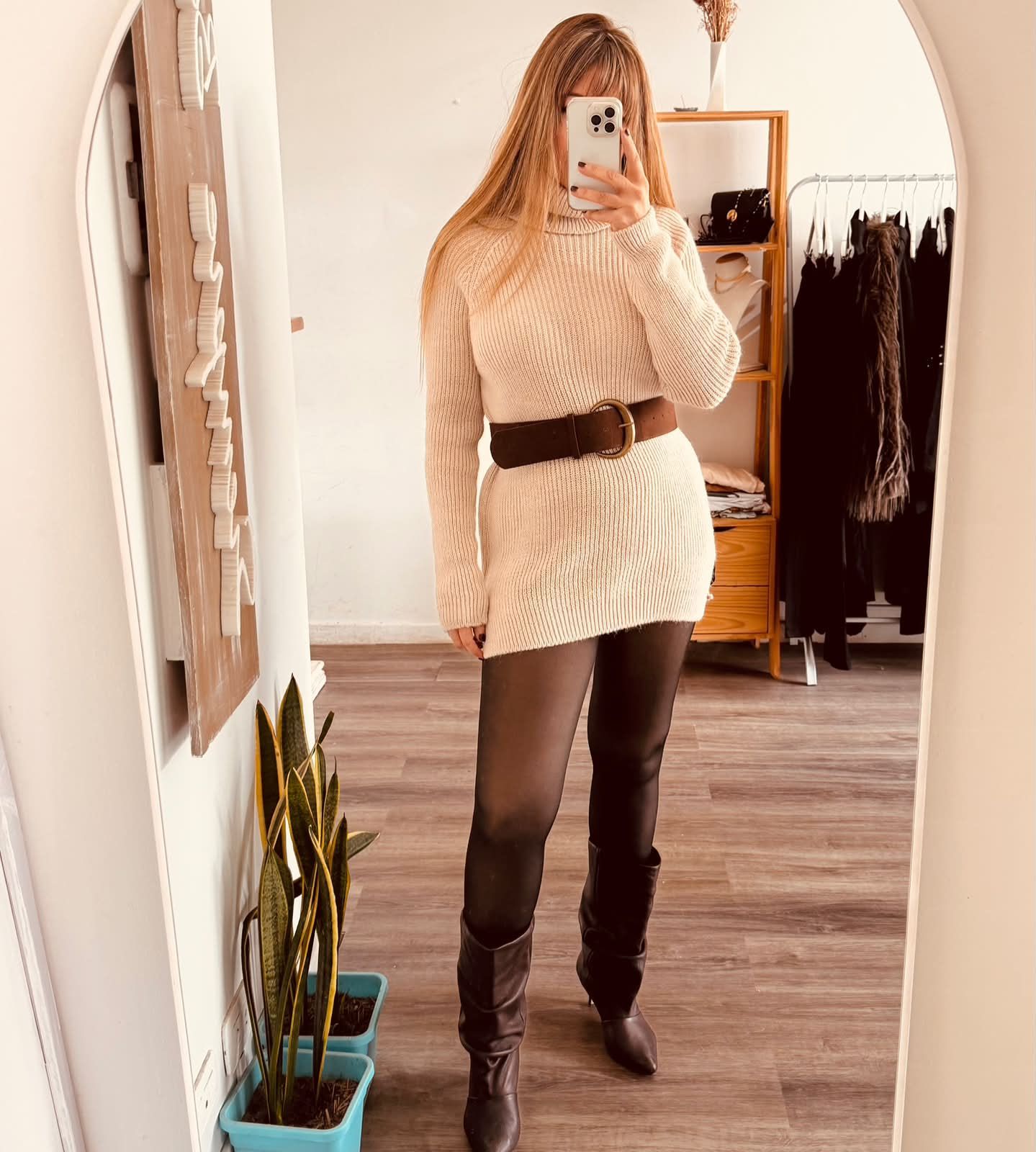 Una persona se toma una selfie frente al espejo con un vestido de punto beige, cinturón marrón,.
