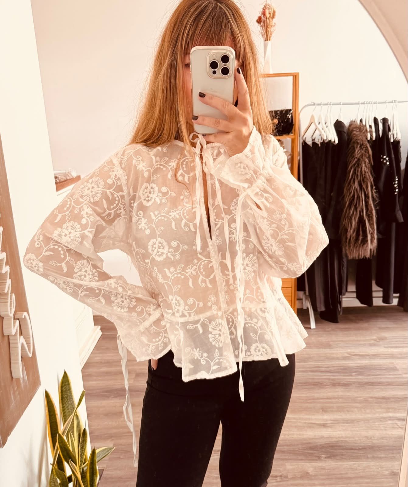 Una persona se toma una selfie frente al espejo, vestida con una blusa blanca de encaje .