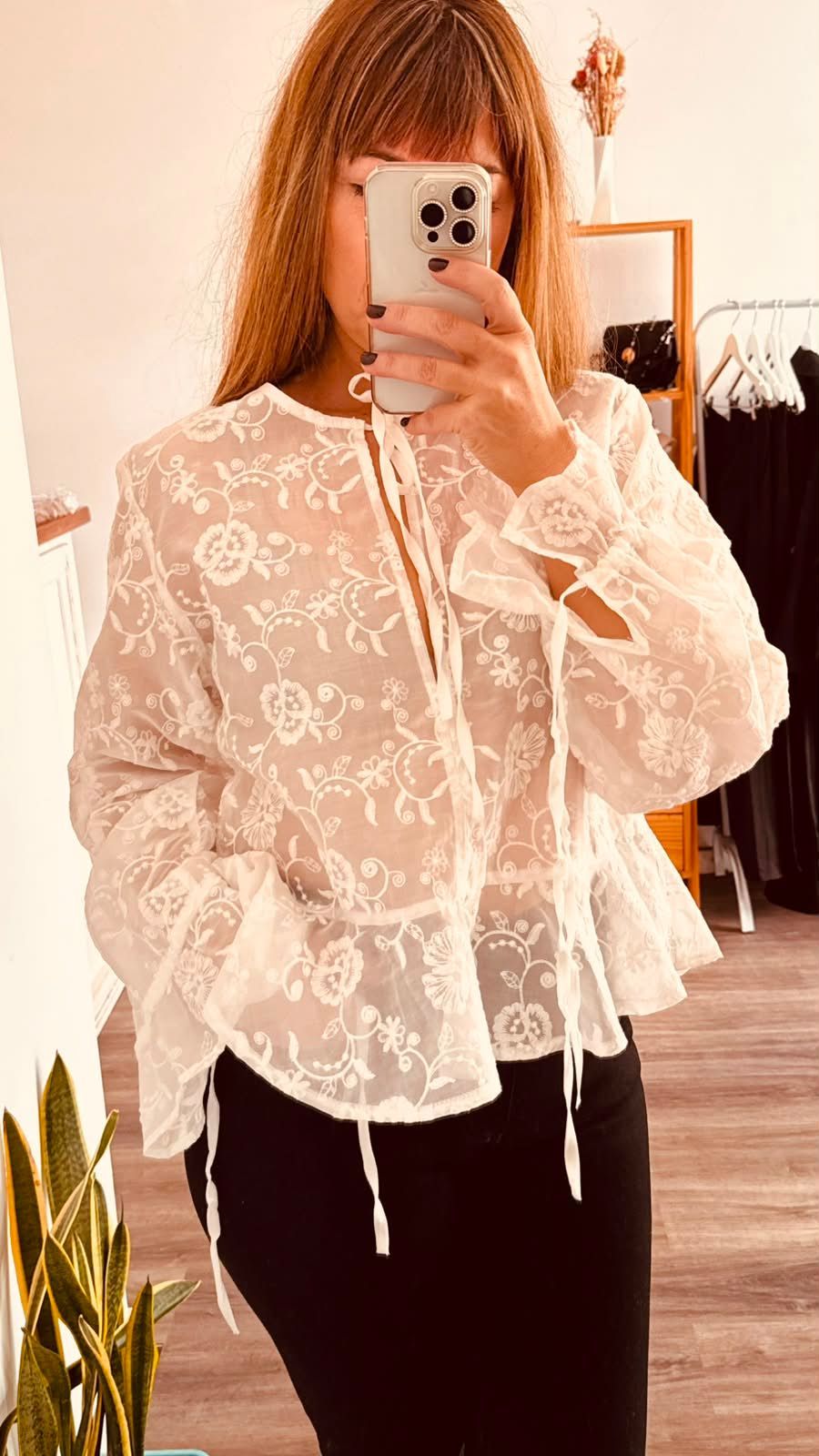 Una persona se toma una selfie frente al espejo, vestida con una blusa blanca de encaje .