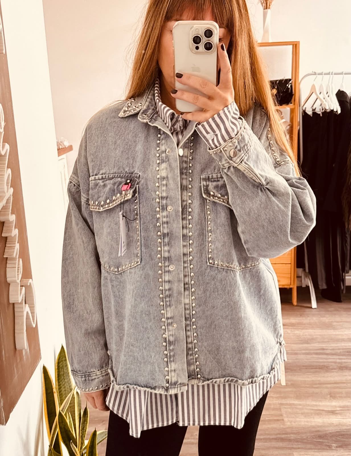 Una persona se toma una selfie frente al espejo con una camisa gris abotonada de gran tamaño sobre una blusa de rayas.
