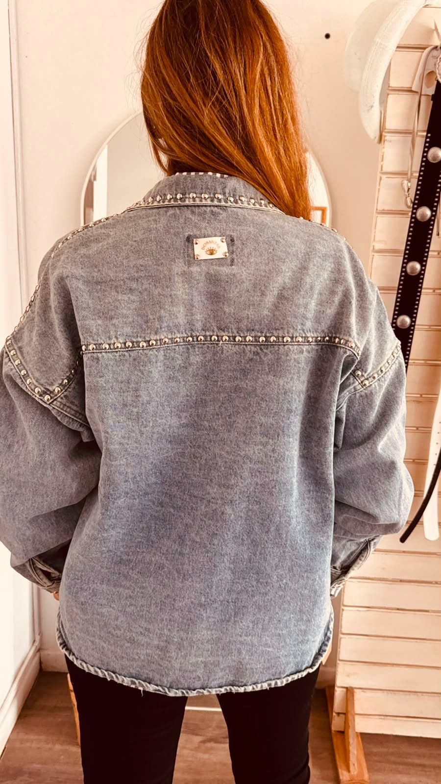 Una persona se toma una selfie frente al espejo con una camisa gris abotonada de gran tamaño sobre una blusa de rayas.