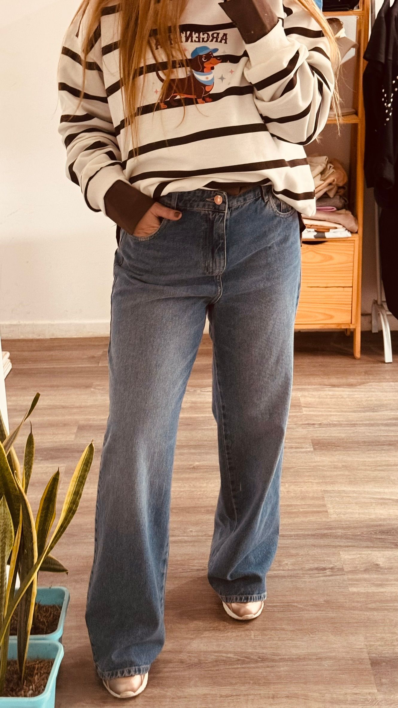 Una persona se toma una selfie frente al espejo con un suéter de rayas y jeans azules en el interior de un edificio.