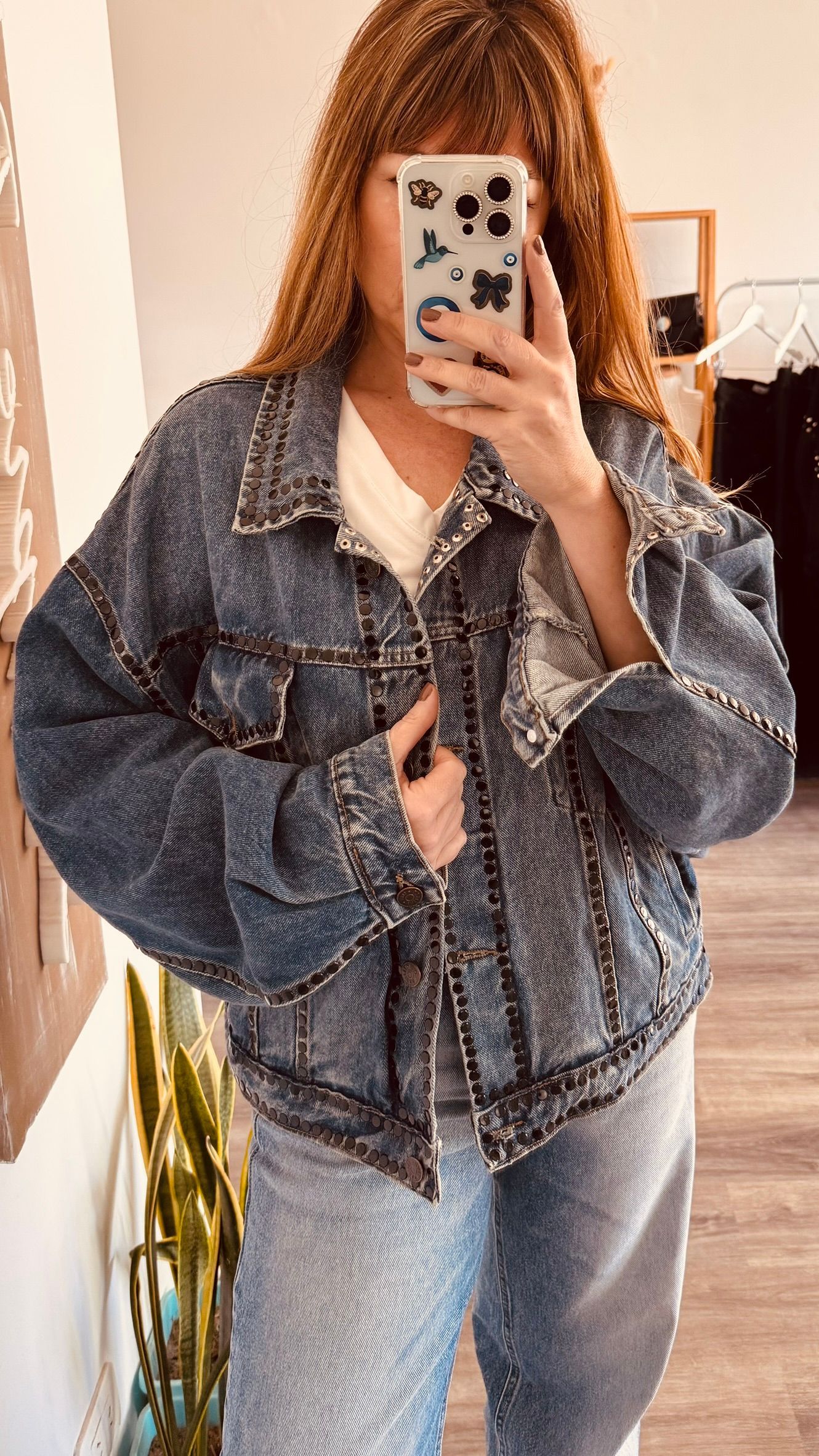 Selfie frente al espejo en una habitación, con chaqueta vaquera y pantalones vaqueros claros, sosteniendo un teléfono.