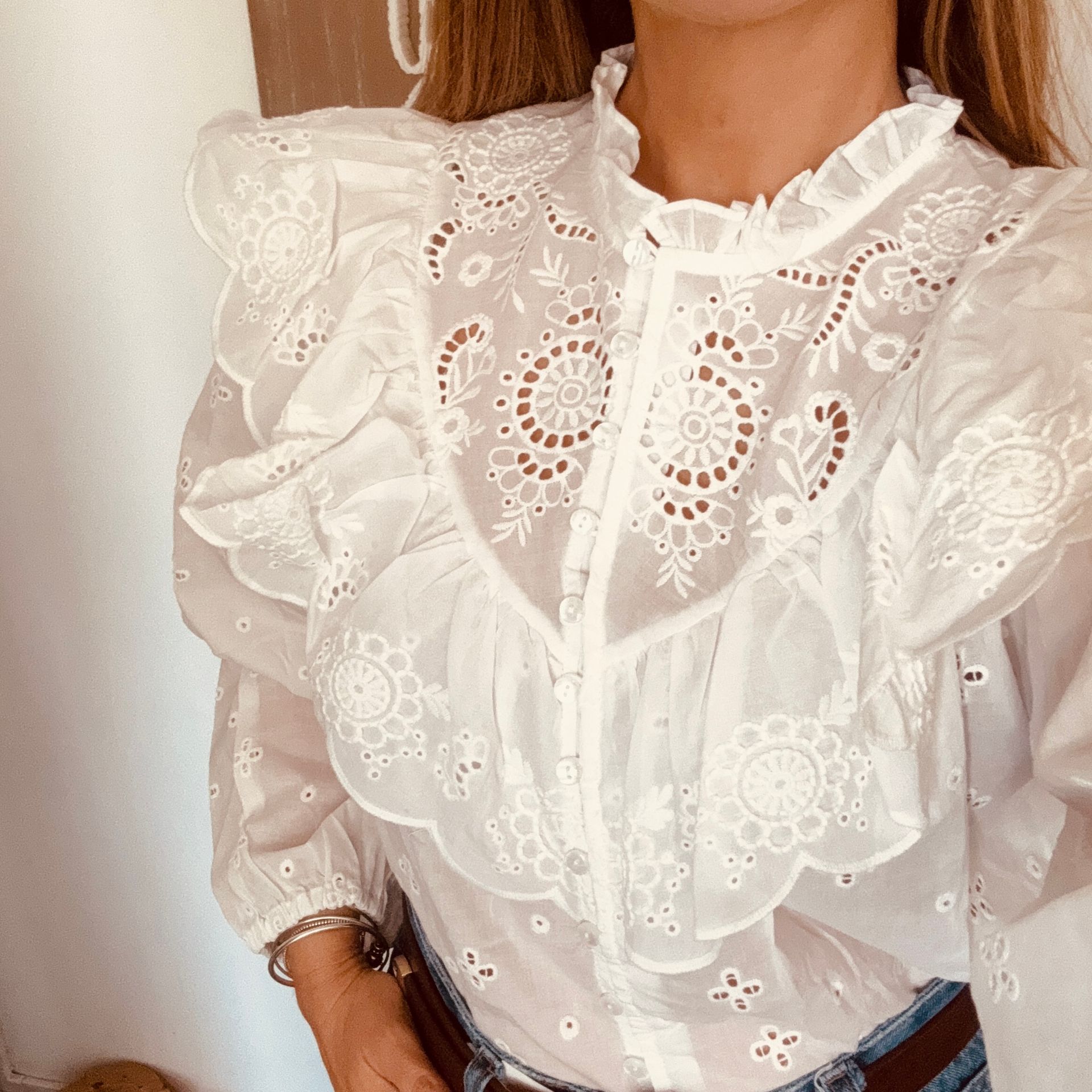Mujer con blusa blanca de encaje con volantes y vaqueros, vista desde los hombros hasta la cintura.