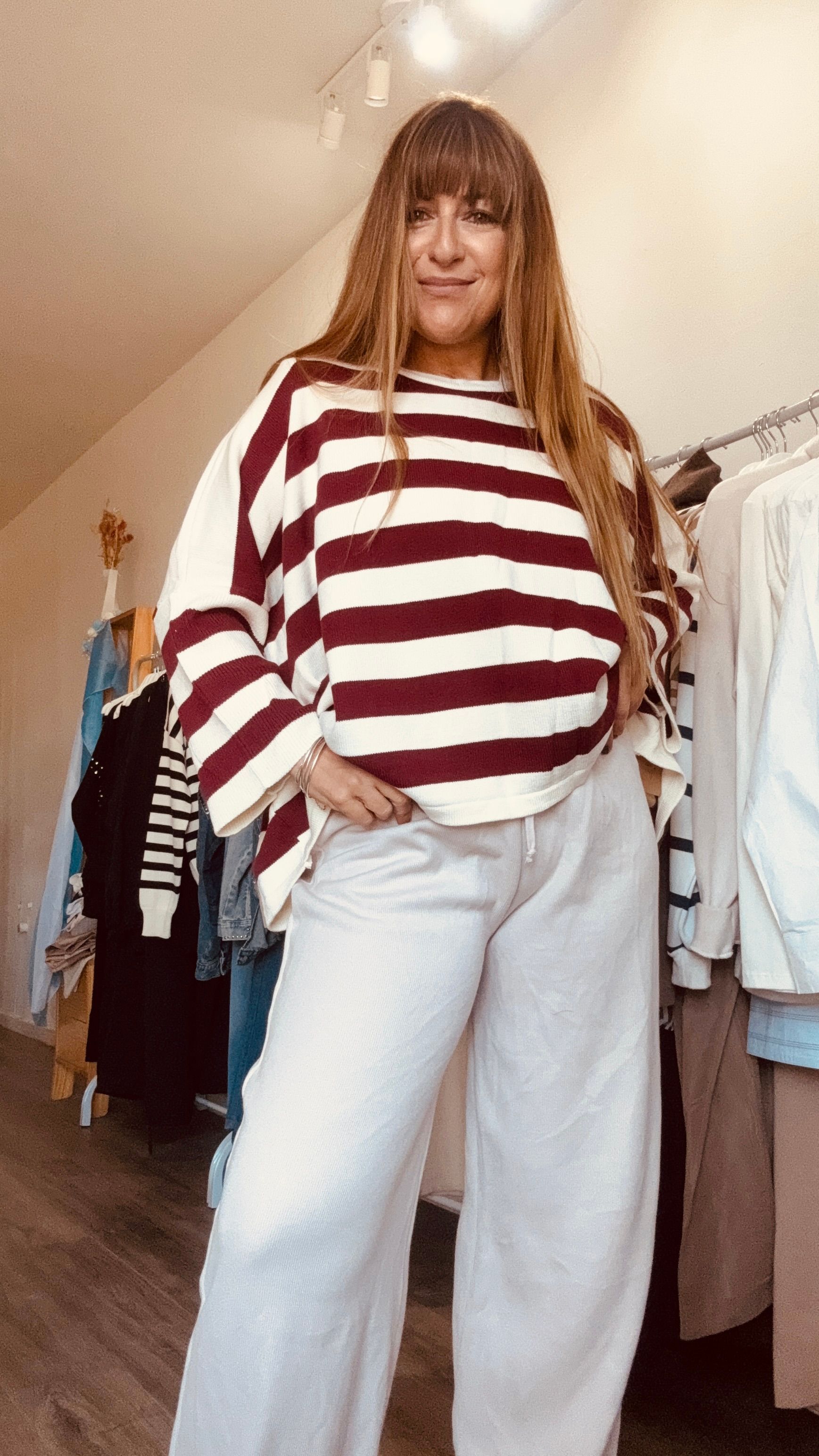 Mujer con suéter de rayas rojas y blancas y jeans claros posando en una tienda de ropa.
