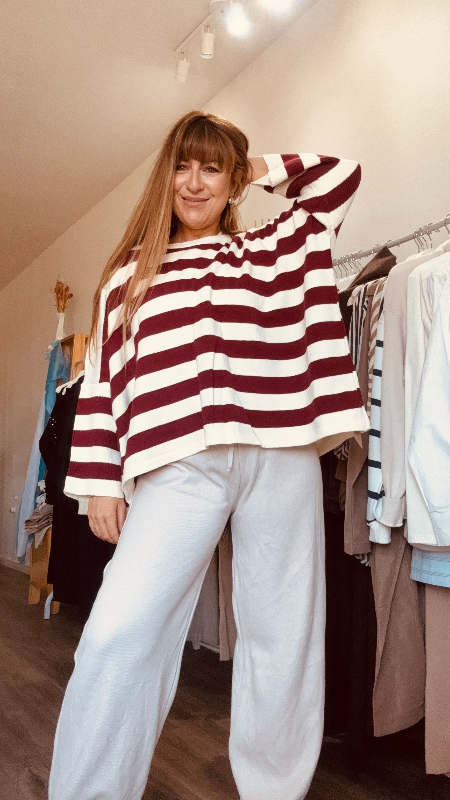 Mujer con suéter de rayas rojas y blancas y jeans claros posando en una tienda de ropa.
